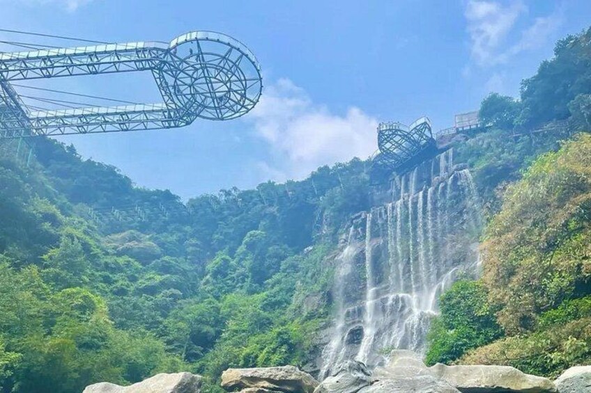 A waterfall cascading down a lush green hillside, with a large metal structure in the background. 4