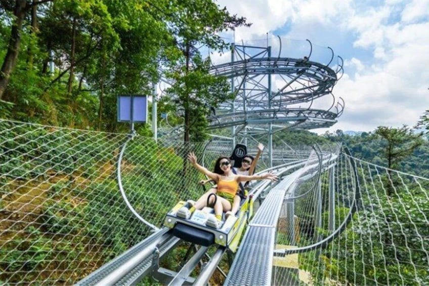 A zipline with two people at the end, surrounded by greenery and a metal structure overhead. 2