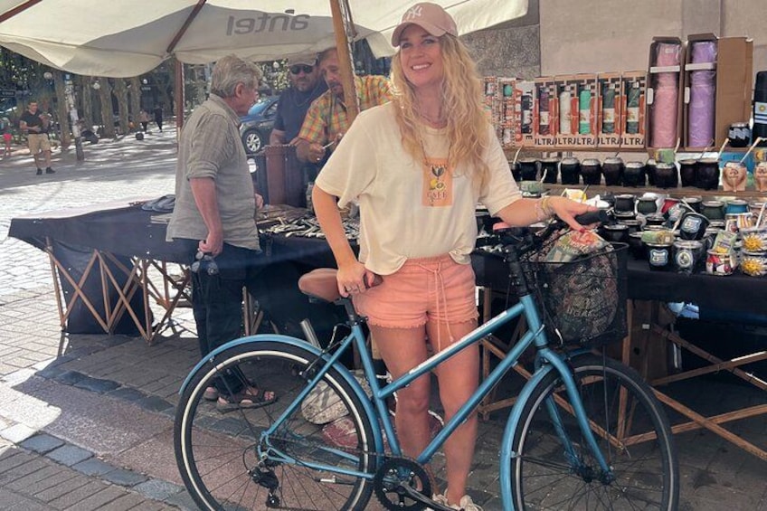 Eine Person steht neben einem blauen Fahrrad, im Hintergrund ist ein Marktstand zu sehen. 1
