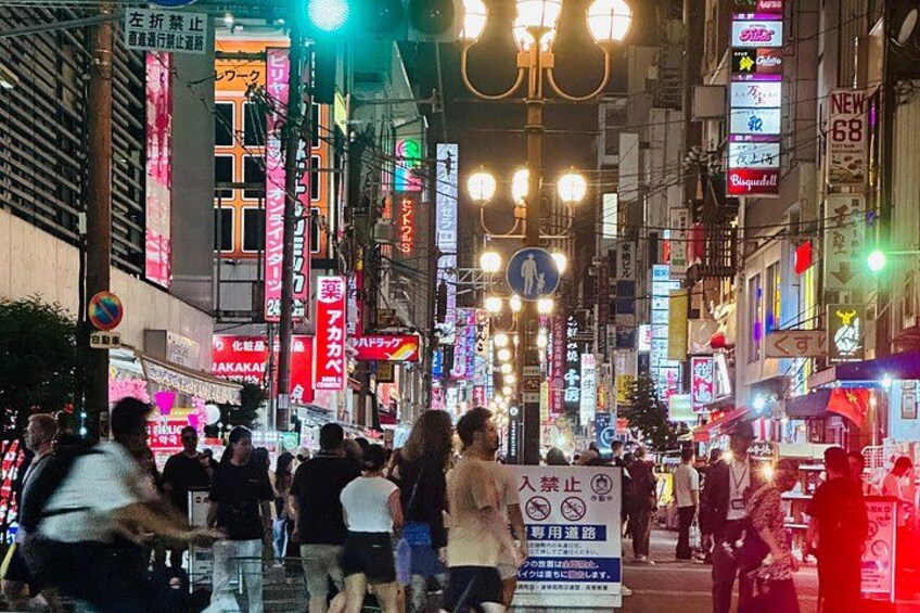 Una calle urbana concurrida en la noche, con letreros iluminados y farolas. 5