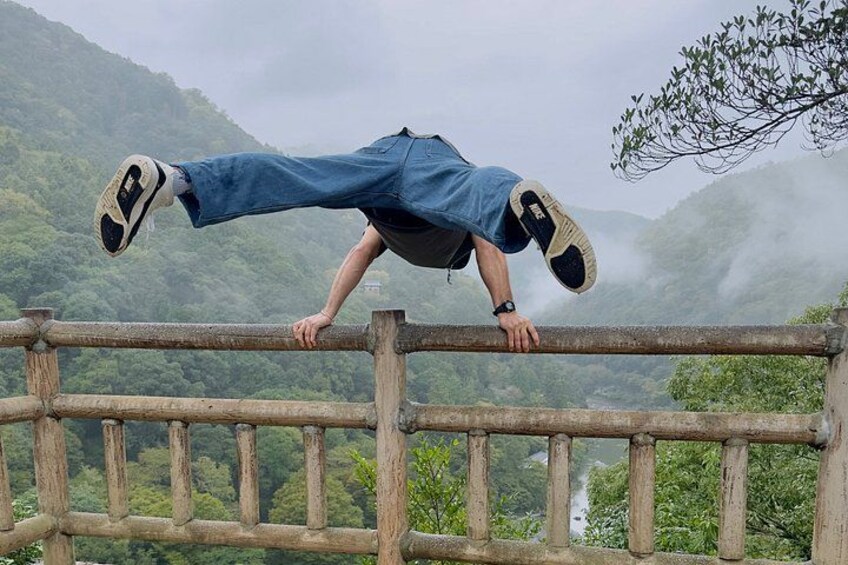 Una persona haciendo una parada de manos sobre una baranda de madera, con un paisaje montañoso de fondo. 2