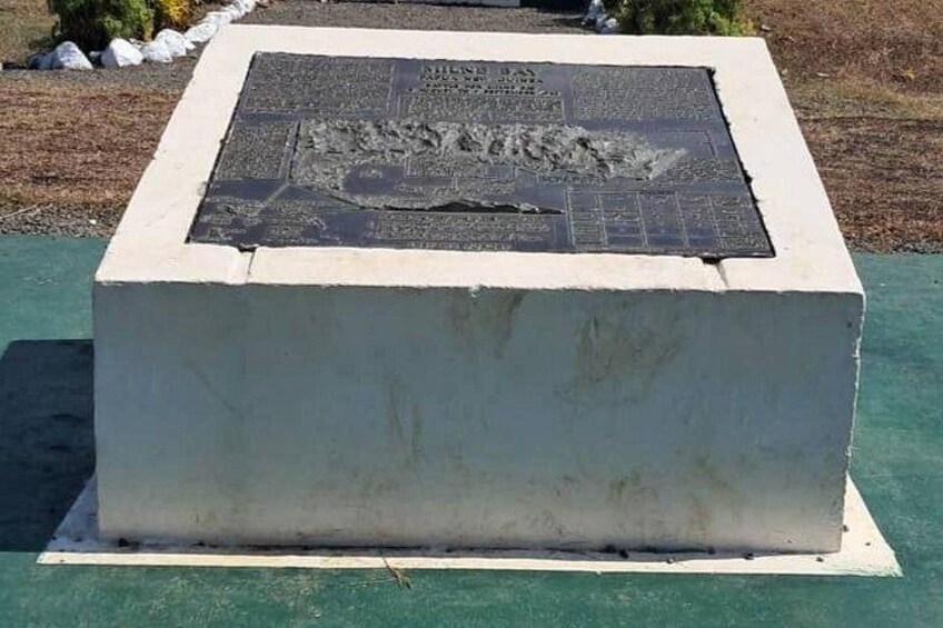 Un monumento de piedra erosionada con inscripciones, rodeado de césped y un sendero pavimentado. 3