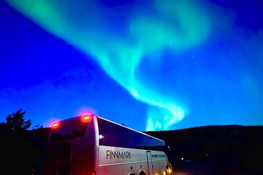 A bus with 'FINNMARK' written on it, parked under a night sky with the Northern Lights. 5