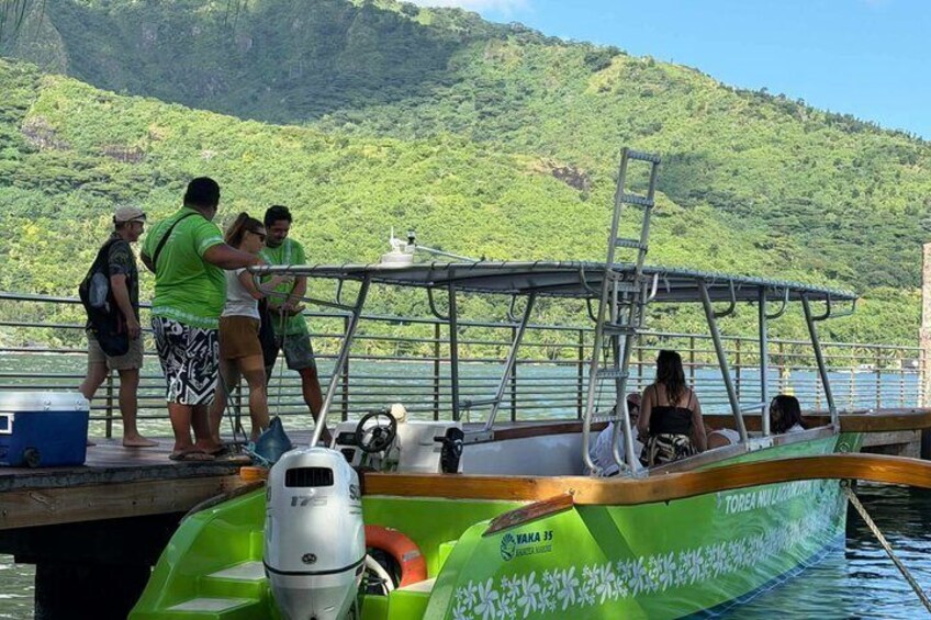 Un bote verde amarrado a un muelle, con gente abordando y desembarcando, rodeado de exuberantes colinas verdes. 5