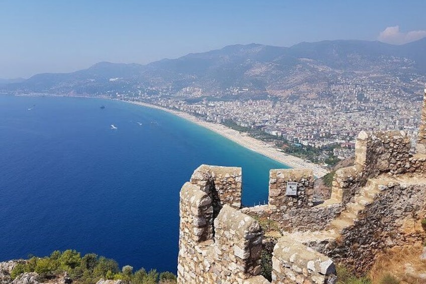 A coastal city with a clear blue sea, a sandy beach, and a stone fortification. 4