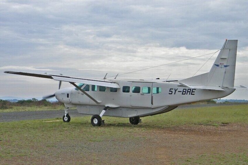 A small white aircraft with the registration number 5Y-BRE parked on a grassy field. 3