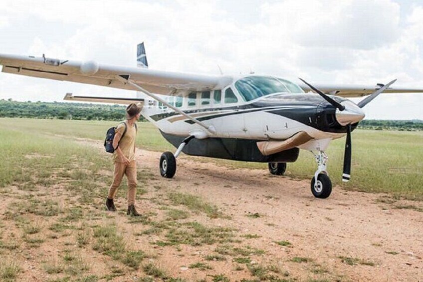 A small aircraft on a dirt runway with a person standing beside it. 4