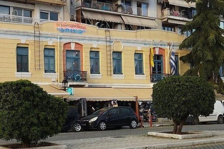 A yellow building with balconies and flags, a parked car, and a tree in the foreground. 3