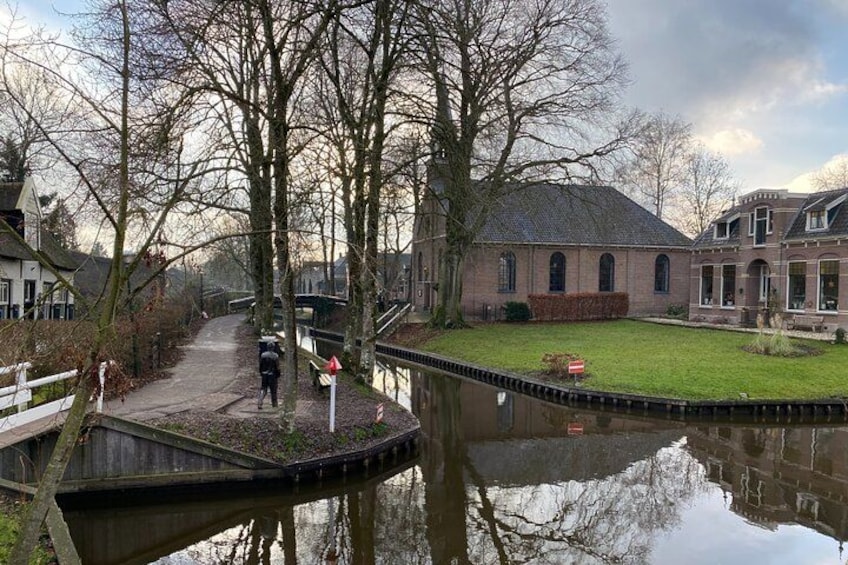 A canal with a bridge, a person walking, and a building with a garden. 2