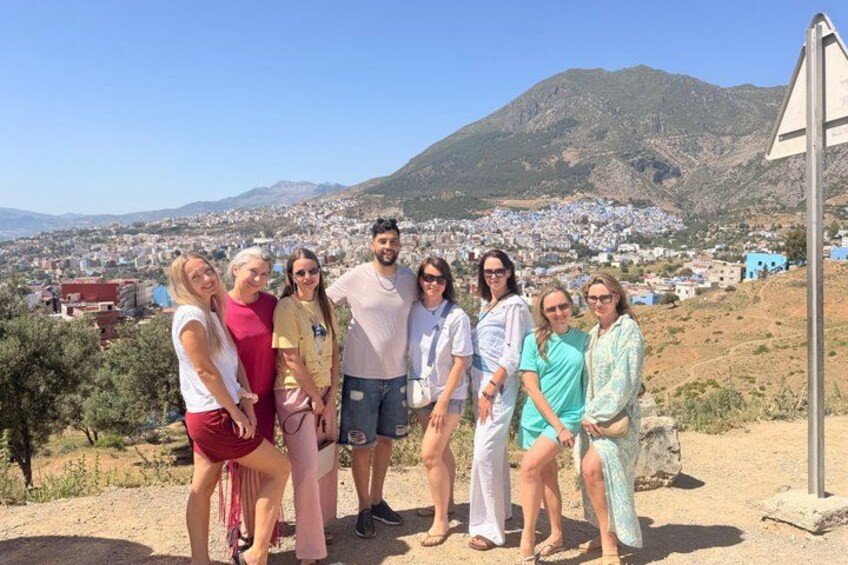 A group of people standing on a hillside with a town and mountains in the background. 5
