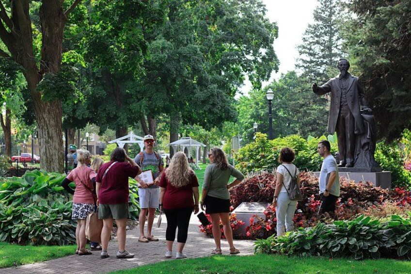 Un groupe de personnes se tient debout et discute dans un parc, près d’une statue et au milieu d’une végétation luxuriante. 3