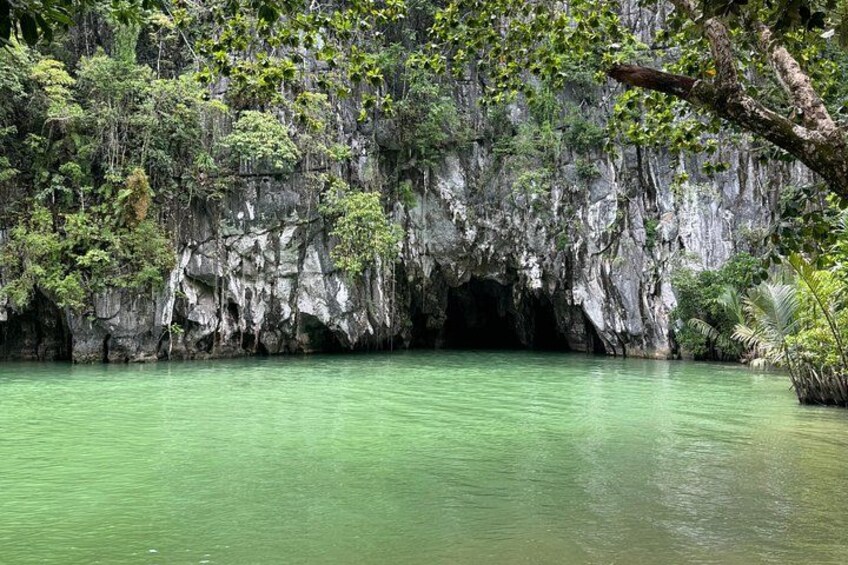 Eingang zu einer Höhle, umgeben von üppiger Vegetation und einem ruhigen Gewässer. 5