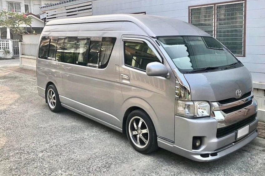A silver van parked on a gravel driveway in front of a house with a window and a door visible. 2