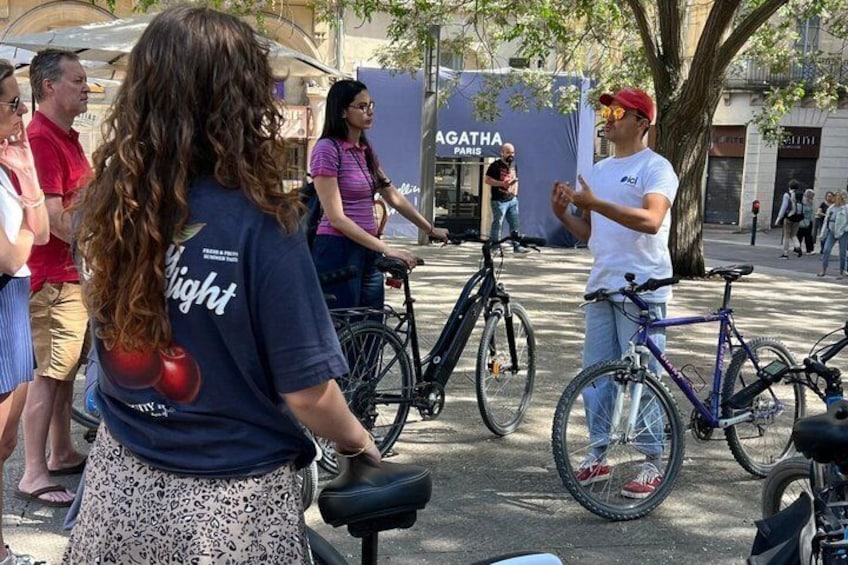 Een groep mensen staat buiten, met fietsen, een spandoek waarop 'AGATHA PARIS' staat en een boom op de achtergrond. 2