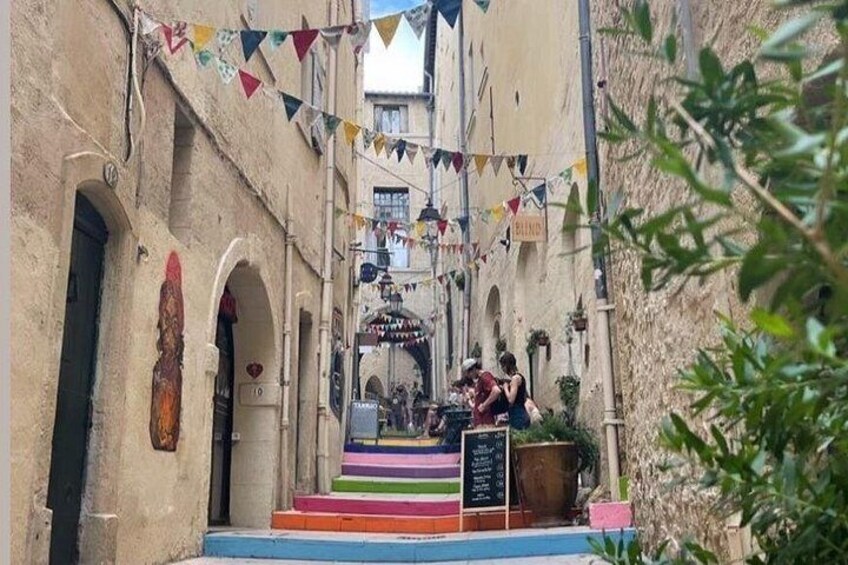 A narrow street with colorful flags, a building with a sign, and a staircase leading to a door. 5
