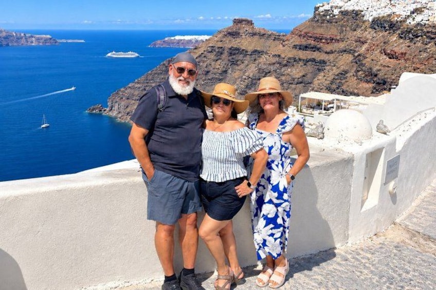 Drei Personen stehen auf einer weiß getünchten Klippe mit Blick auf das Meer, im Hintergrund sind Boote zu sehen. 2