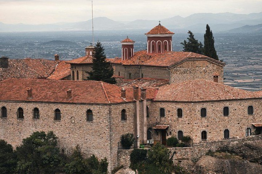 A historic stone building with red-tiled roofs, a bell tower, and a view of the surrounding landscape. 4