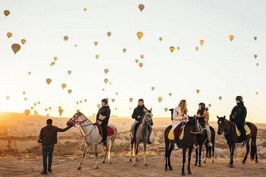 Un grupo de personas a caballo, con globos aerostáticos al fondo. 3