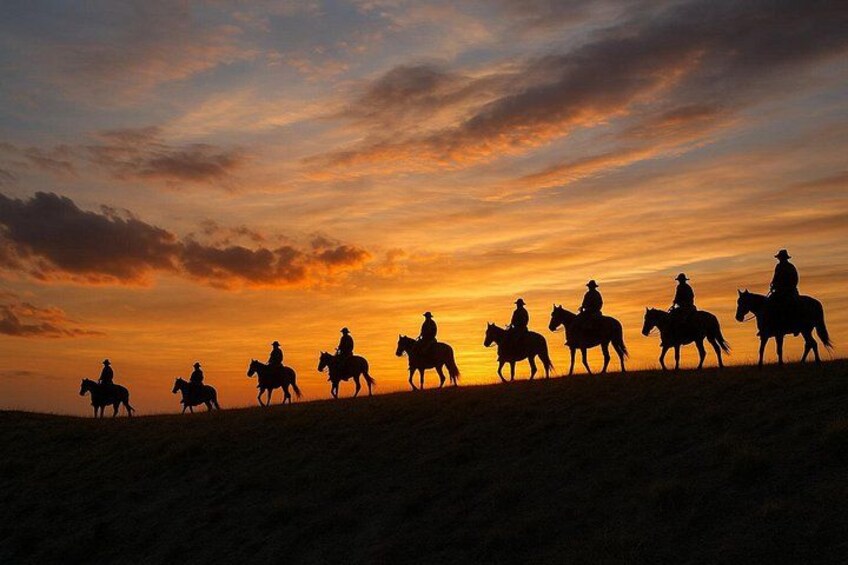 Silhouettes of people on horseback against a sunset sky. 1