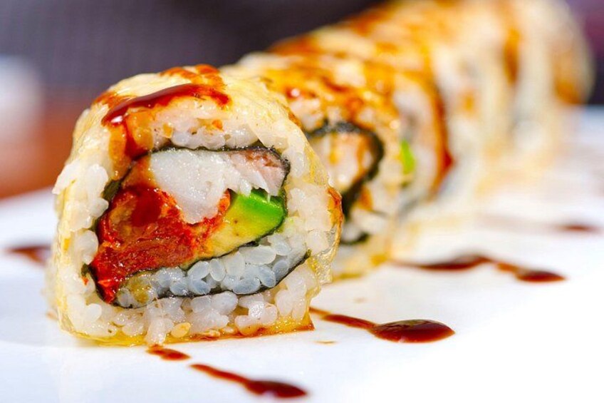 Un rouleau de sushi dont on peut voir les ingrédients, comme le poisson, l’avocat et le riz, et qui est agrémenté d’une sauce. 2