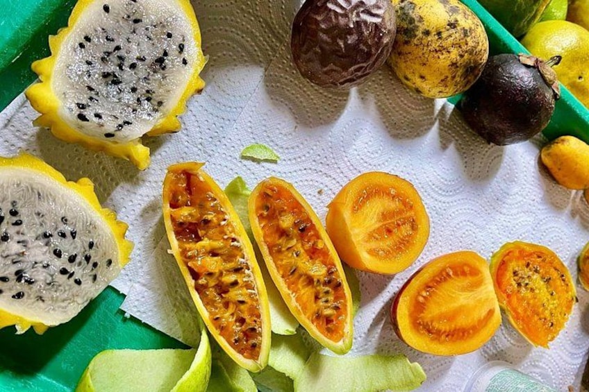 Frugtvariation, herunder dragefrugt, passionsfrugt og guava, nogle skåret og nogle hele, på en grøn bakke. 4