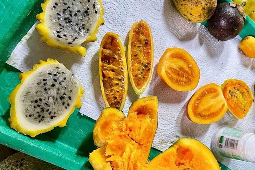 Forskellige frugter, herunder dragefrugt, papaya og passionsfrugt, nogle skåret over og andre hele, arrangeret på en grøn bakke med et hvidt papirhåndklæde under. 2