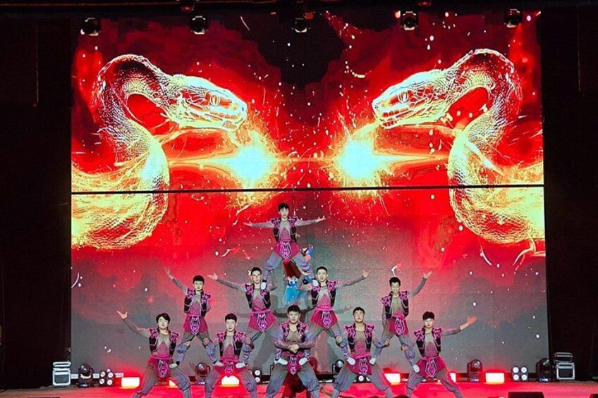 A stage with dancers in colorful costumes performing in front of a large screen displaying a dragon. 4