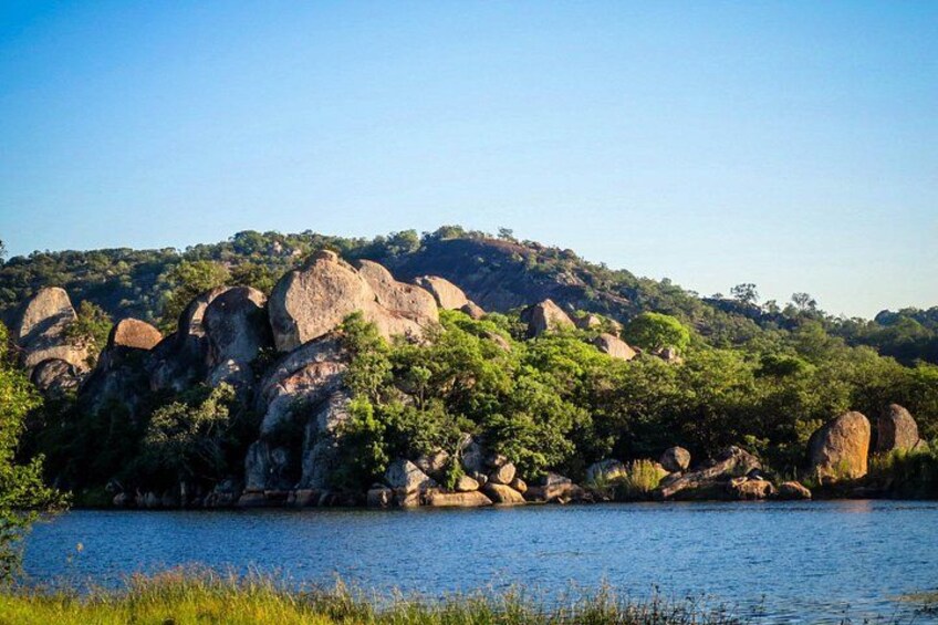 A calm lake surrounded by large boulders and dense greenery. 2