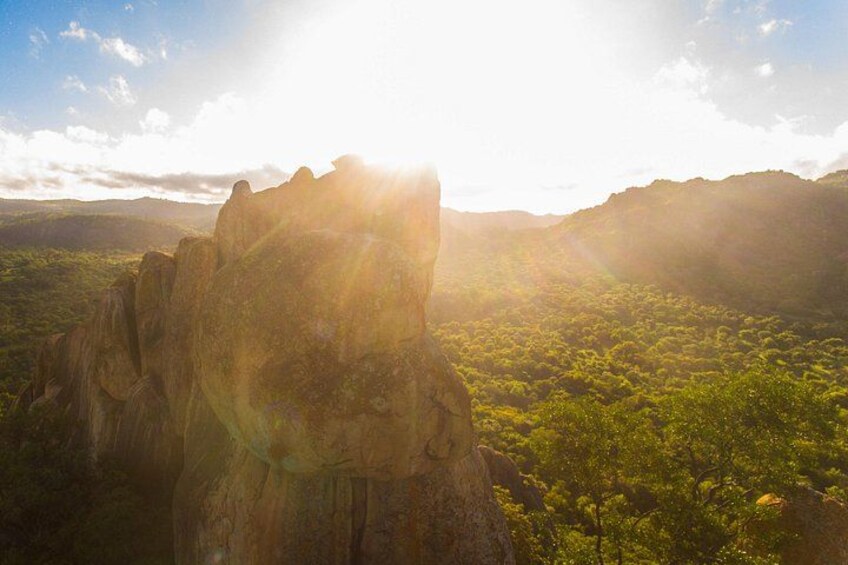 A mountainous landscape with a prominent rock formation and dense green forest. 4