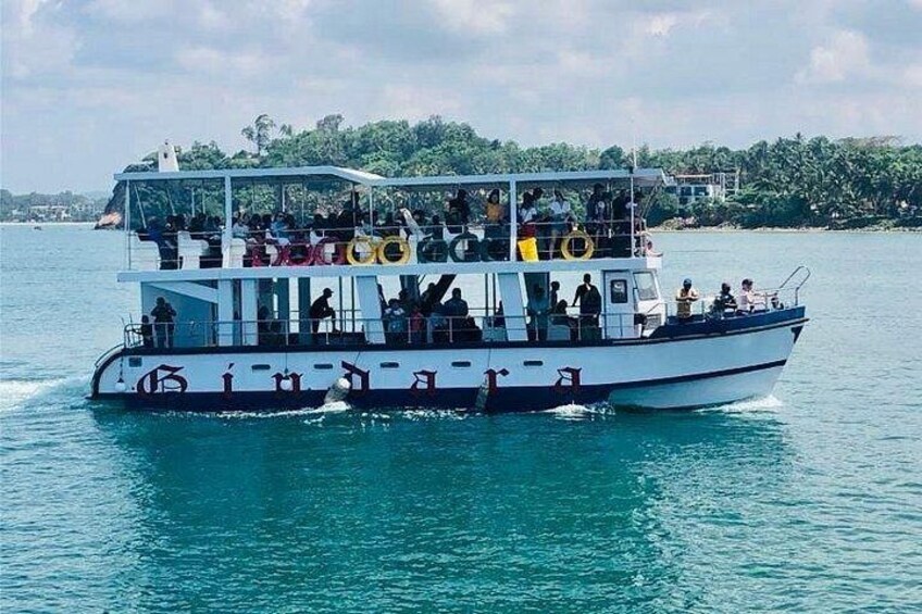 A double-deck boat with passengers on a calm body of water. 1