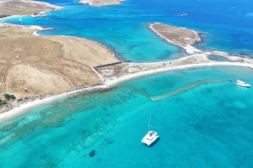 An aerial view of a coastal area with clear turquoise waters, a sandy beach, and a small boat anchored near the shore. 4