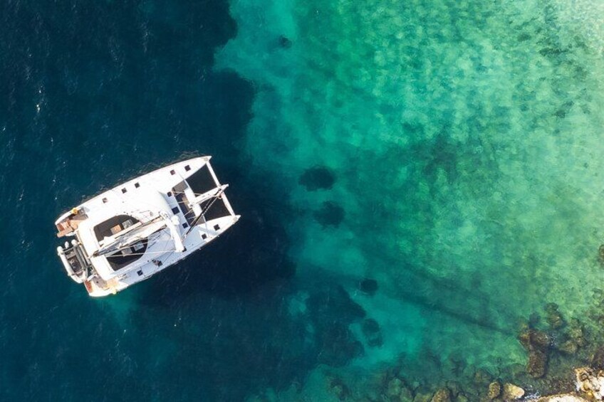 A white boat anchored in clear turquoise waters with visible underwater rocks. 1