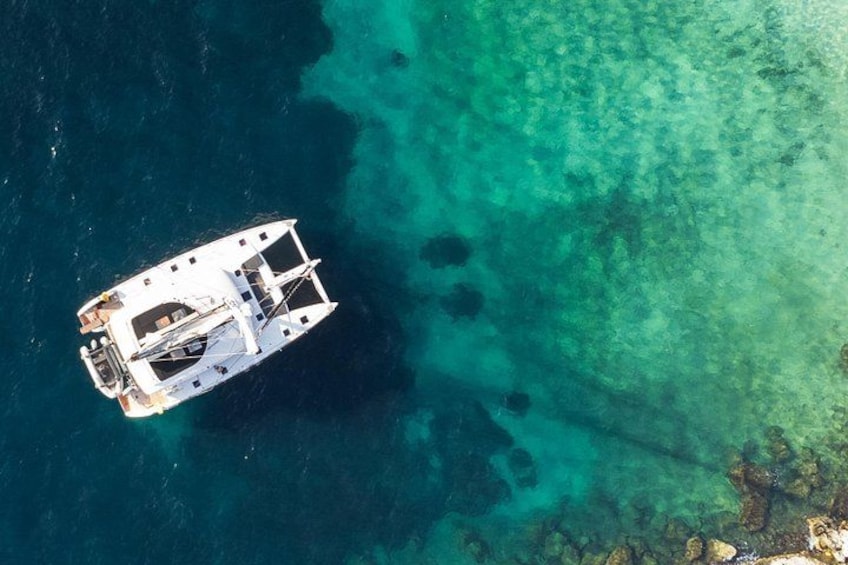 A boat in clear turquoise waters with a rocky shoreline in the background. 1