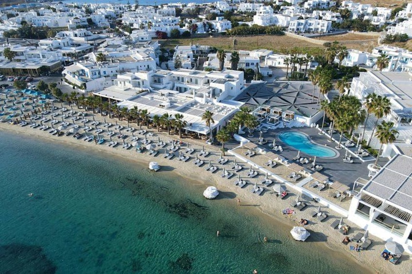 An aerial view of a coastal resort with white buildings, a beach, and a swimming pool. 5