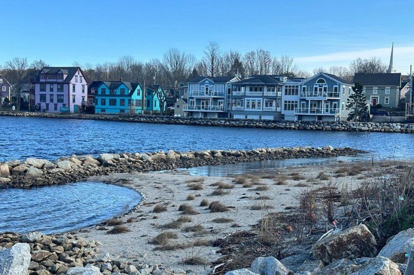 A waterfront with colorful houses, a rocky shoreline, and a clear blue sky. 2