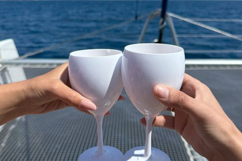 Two hands holding white wine glasses on a boat deck with a blue ocean in the background. 3
