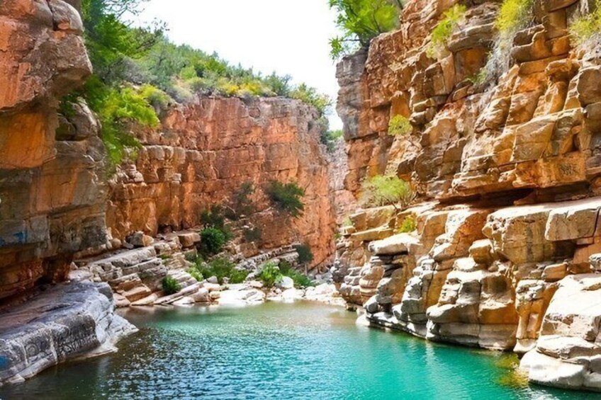 Een canyon met een turquoise poel, omgeven door rotsachtige kliffen en schaarse begroeiing. 5
