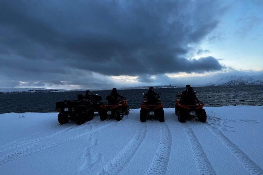 Tre ATV'er parkeret på sneklædt jord med et vandareal og bjerge i baggrunden. 5