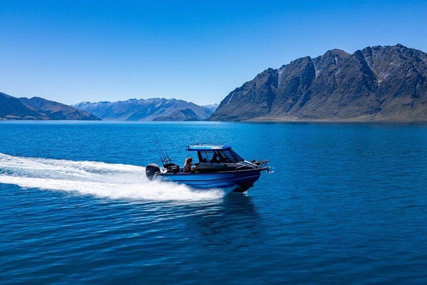 A blue boat speeding across a calm lake with mountains in the background. 5