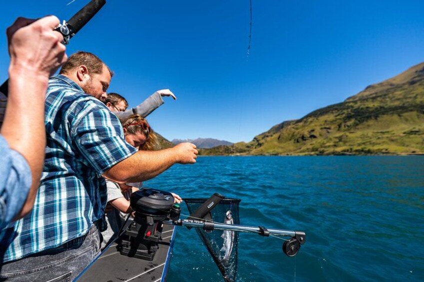 People fishing on a boat with a clear blue lake and hills in the background. 3