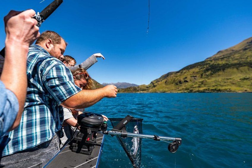 People fishing on a boat with a clear blue sky and hills in the background. 2