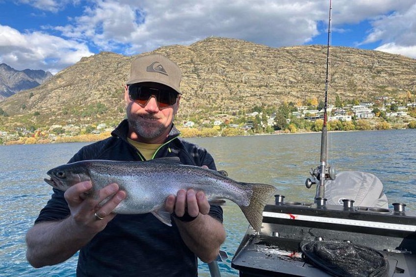 A person holding a fish by a lake with mountains in the background. 3