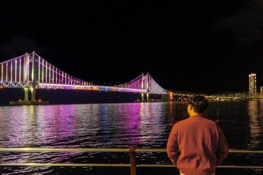 A brightly lit bridge at night with reflections on the water. 4