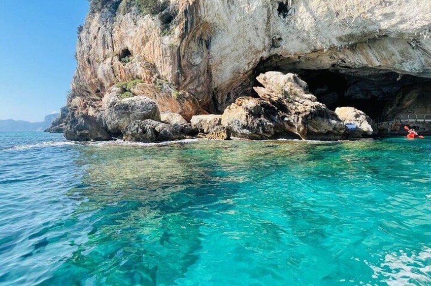 A clear blue sea, rocky cliffs, and a cave entrance. 4