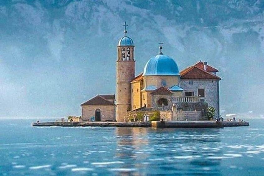 A church with a blue dome and a bell tower on a small island surrounded by water. 3