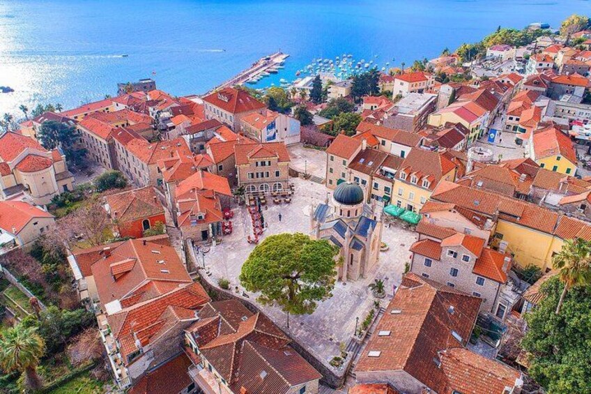 A coastal town with red-roofed buildings, a central square with a dome structure, and a clear view of the sea. 5
