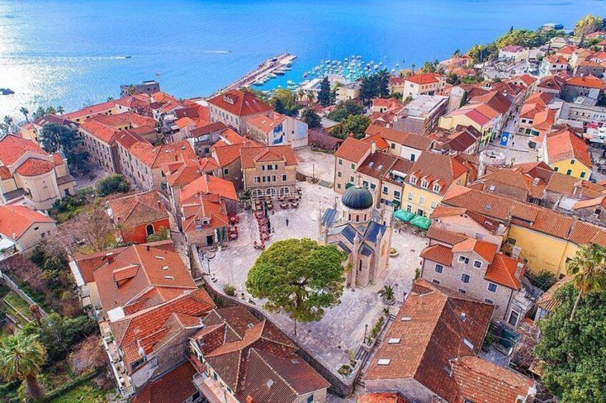 A coastal town with red-roofed buildings, a central square with a dome structure, and a clear view of the sea. 2