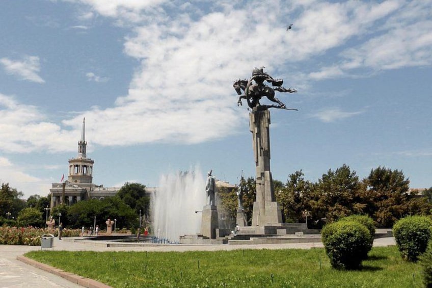 A park with a fountain, a statue, and a building with a tower. 5
