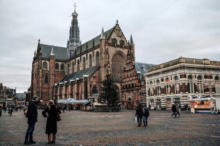 En historisk kirke med et højt spir, et marked med boder, og en traditionel bygning med buede vinduer. 2