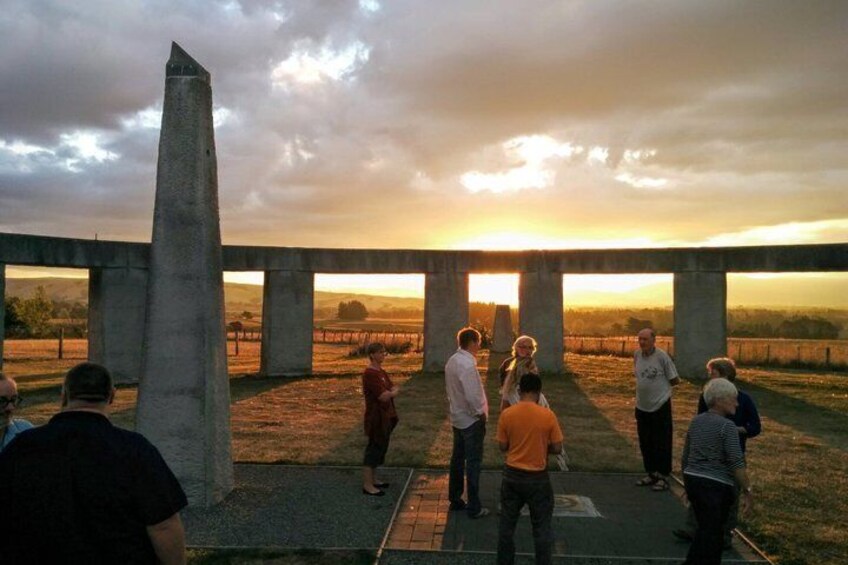 A group of people standing under a structure with a sunset in the background. 1